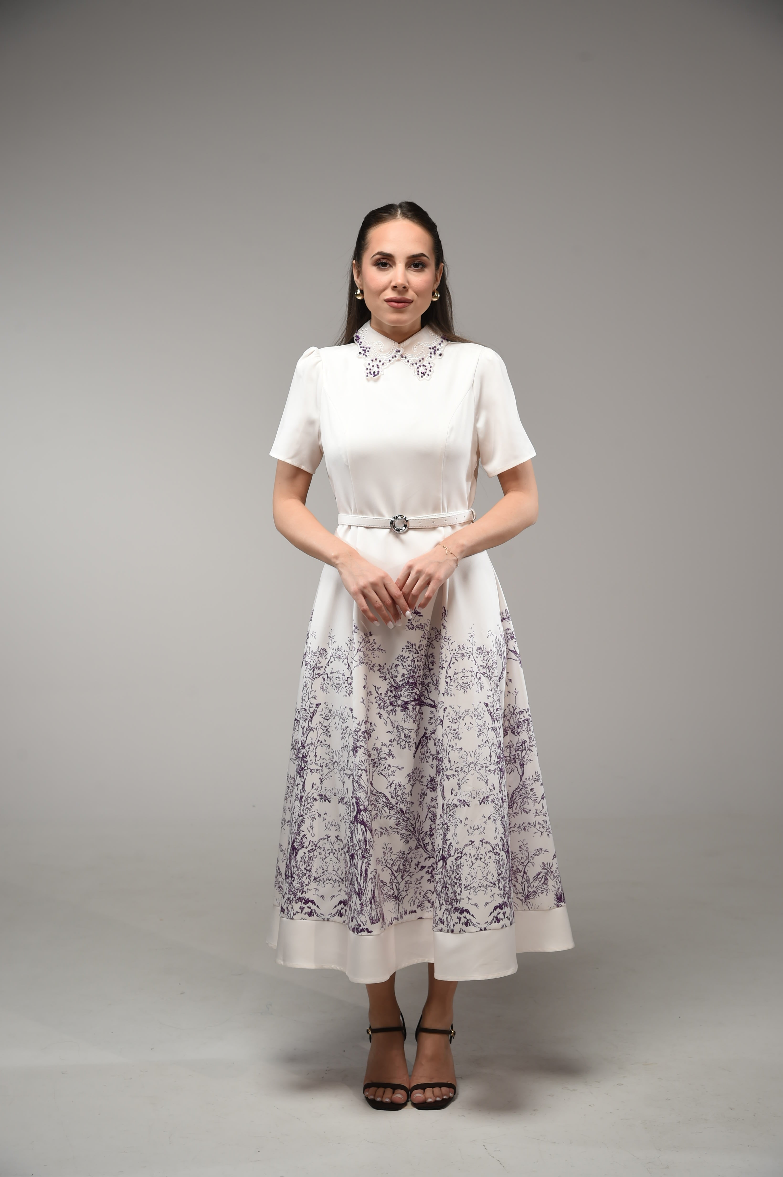 Woman wearing a white dress with floral patterns on a gray background